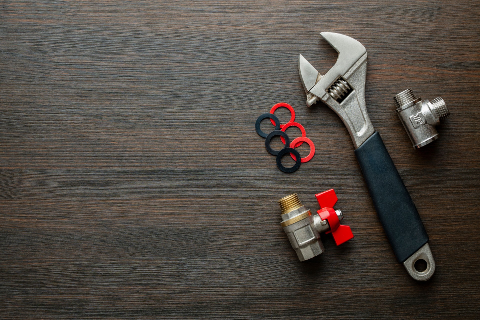 Metal adjustable wrench, ball valve with red handle, stainless steel tee fittings and rubber gaskets on wooden background, closeup, top view, copy space. Plumbing repair concept